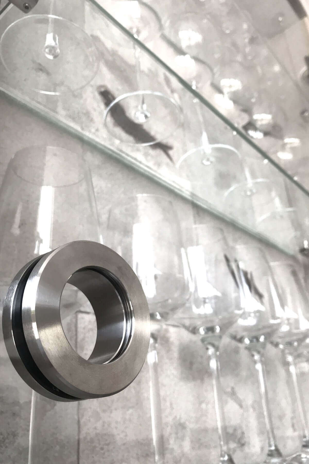 Close-up of a stainless steel ring beside an elegant row of wine glasses on a glass shelf.